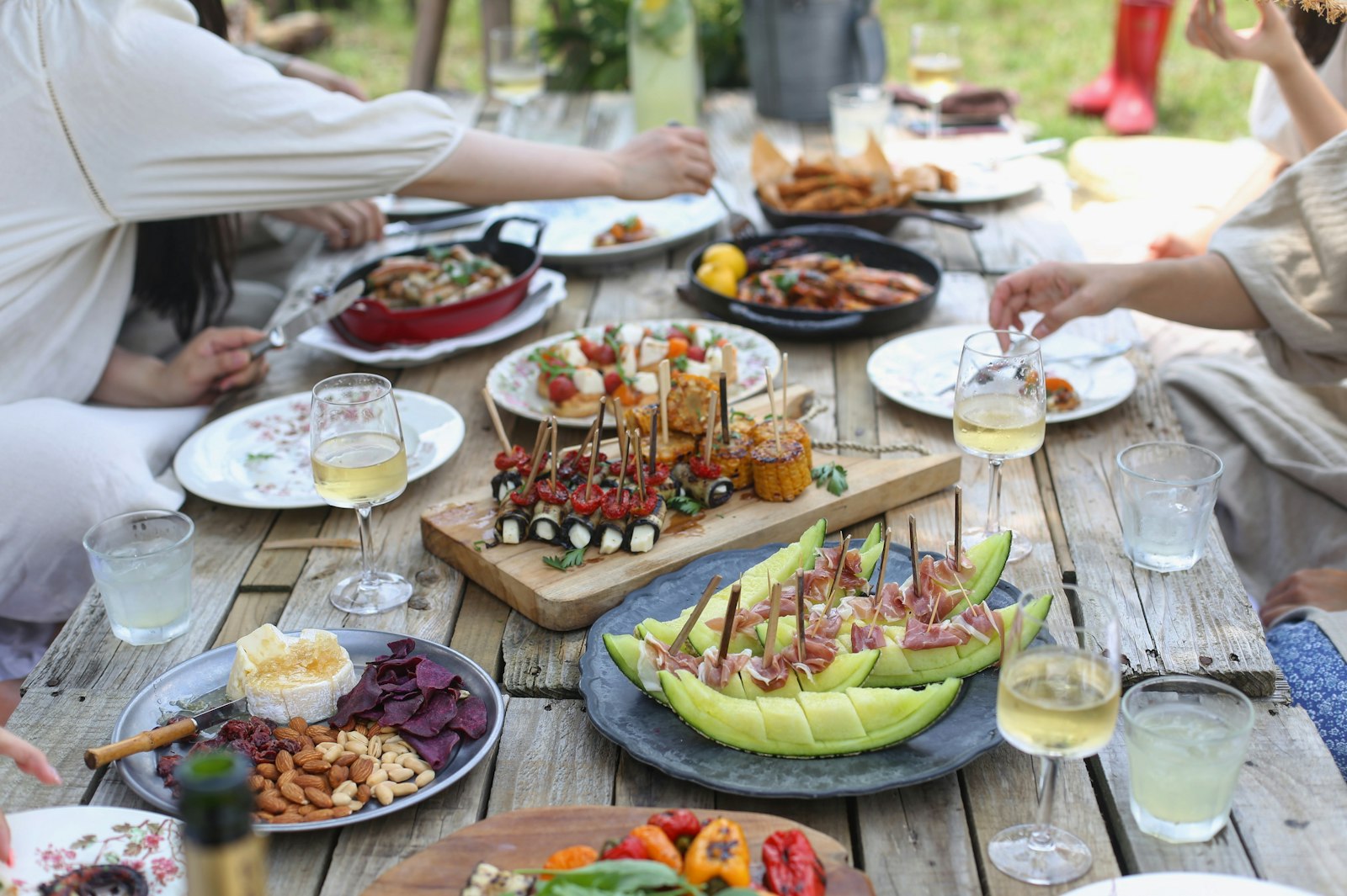 A weathered wooden table set with linen, shared plates, and reaching hands at an unhurried lunch.