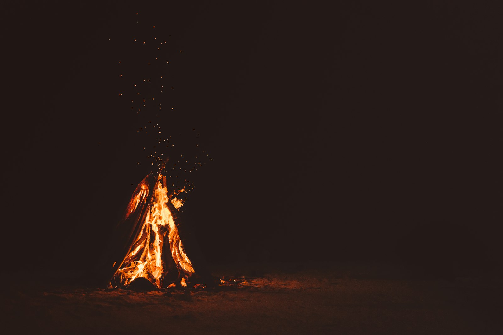 A bonfire burning against pure darkness, sparks rising.